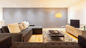 Een moderne woonkamer met een modulaire bank, een salontafel en een televisie op een wit kastje.