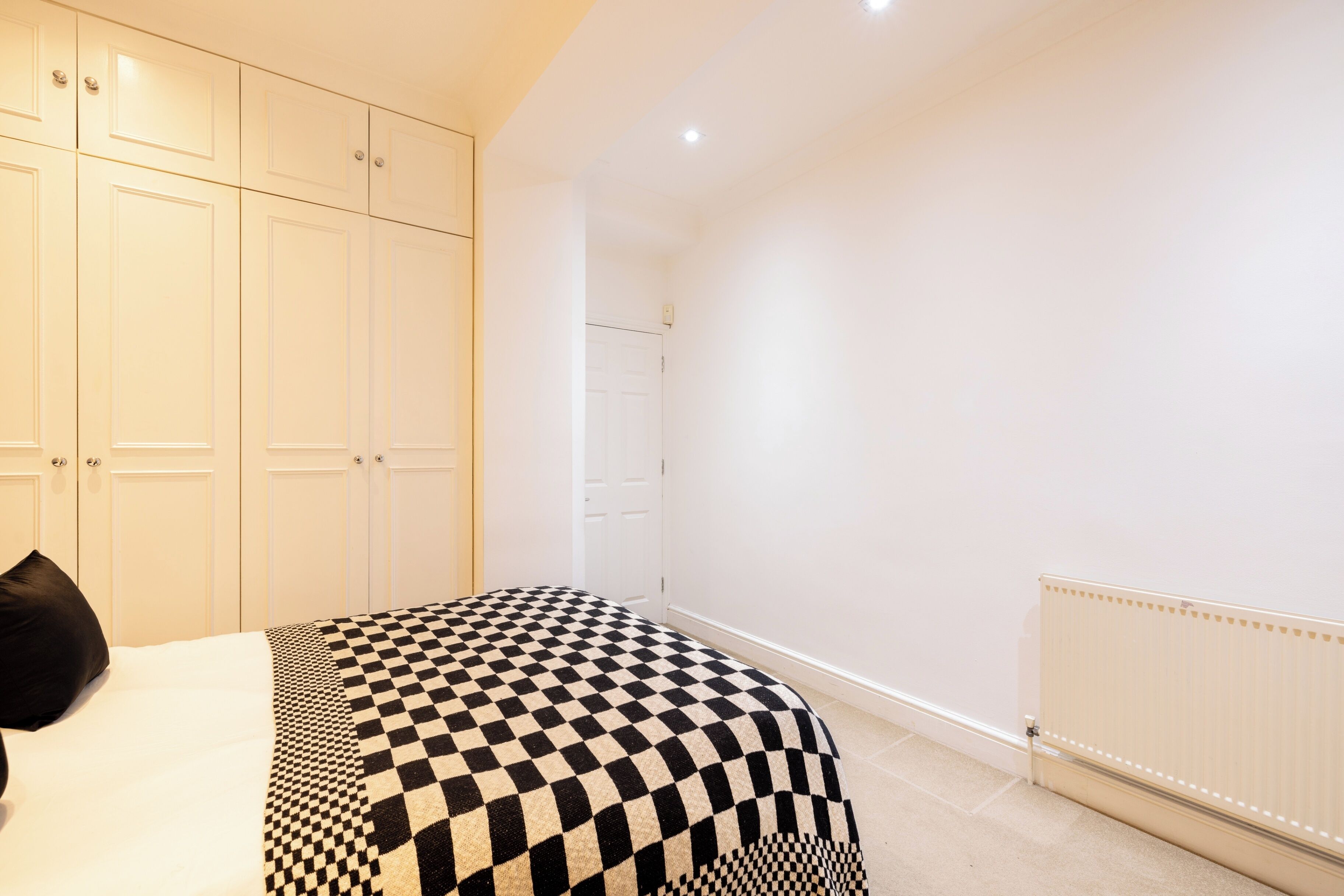 Une chambre à coucher avec une couvre-lit à carreaux, une porte blanche et un radiateur.