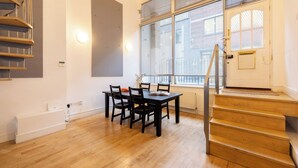 Een modern appartement met een eethoek, een houten trap en grote ramen.