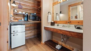 A compact bathroom with a wooden vanity, a sink, a mirror, and a small refrigerator.