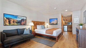 A bedroom with a wooden bed, a gray sofa, and a wooden floor.