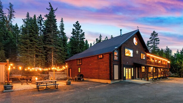 A wooden lodge with a porch and outdoor seating area, surrounded by trees.