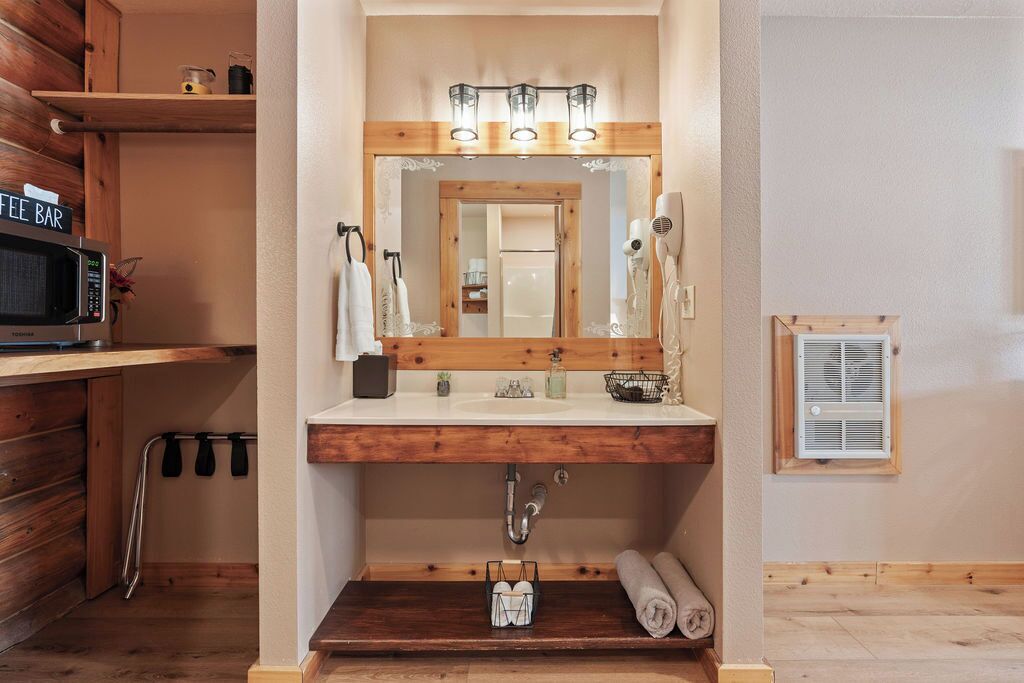 A bathroom with a wooden vanity, a mirror with lights, a towel rack, a sink, and a microwave on a shelf.