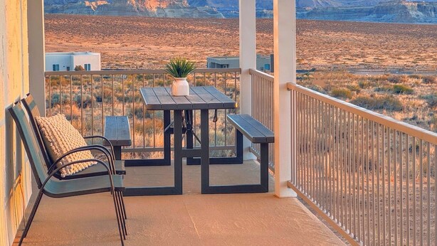 A balcony with a table and chairs, a potted plant, and a view of a desert landscape with mountains in the background.