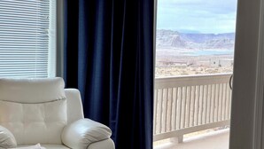 A room with a white leather chair, a dark curtain, and a view of a balcony with a wooden railing.
