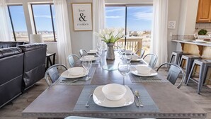 A dining area with a long table set for six, surrounded by chairs, with a view of the landscape through large windows.