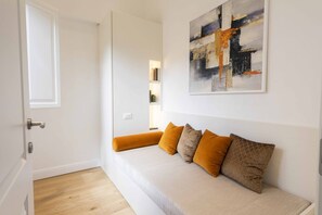 A room with a white wall, a sofa with orange cushions, and a painting above the sofa.