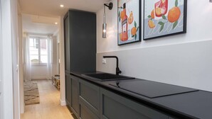 A modern kitchen with a black countertop, a sink, and a dark cabinet. There are two framed pictures on the wall.