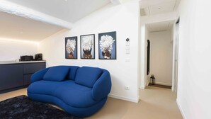 A modern living room with a blue sofa, a black rug, and three wall-mounted flower paintings. - LVL2 By MMega Homes & Villas (Firenze)
