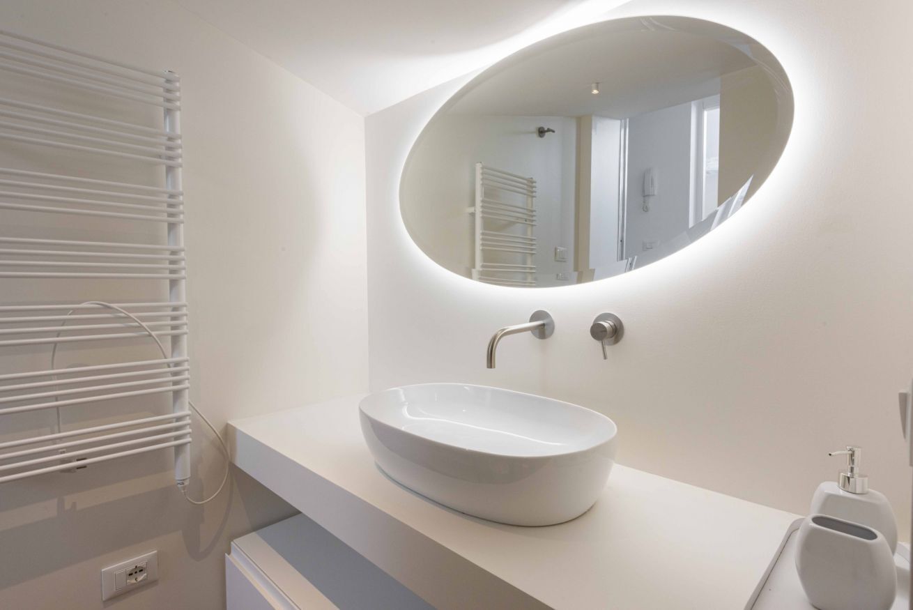 Une salle de bain moderne avec un lavabo blanc, un miroir rond et un porte-serviettes.