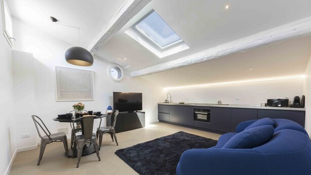 A modern loft apartment with a dining area, a blue sofa, a kitchen, and a skylight. - LVL2 By MMega Homes & Villas (Firenze)