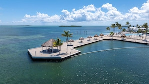 Ein Resort mit Poolbereich, Liegestühlen und einer kleinen Insel mit strohgedeckten Sonnenschirmen.