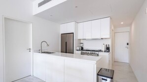 A modern kitchen with white cabinetry, a stainless steel sink, a built-in stove, and a compact trash bin.