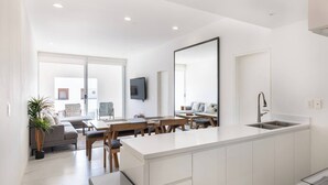 A modern kitchen with a central island, a dining area with wooden furniture, a large mirror, and a TV mounted on the wall.