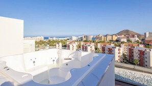 A rooftop with a hot tub, a view of a coastal cityscape, and a mountain in the distance.