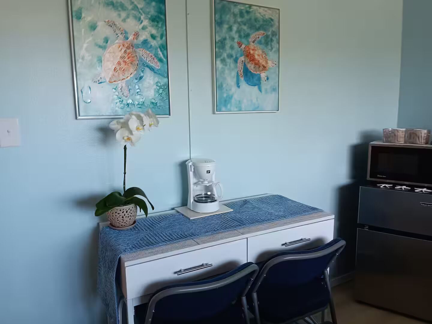 Une petite cuisine équipée d’une machine à café, de deux chaises et d’un four à micro-ondes.