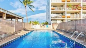 Une piscine à l’eau d’un bleu limpide, entourée d’une clôture et bordée d’un bâtiment doté de balcons.