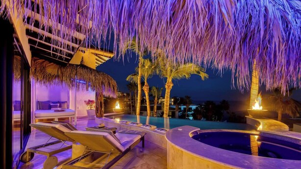 Un espace piscine extérieur luxueux, doté de chaises longues, d  ’un jacuzzi et d’une structure à toit de chaume.