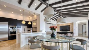 Une cuisine moderne équipée d’appareils électroménagers en acier inoxydable, un coin repas avec une table et des chaises en verre, et un salon doté d’un téléviseur à écran plat.