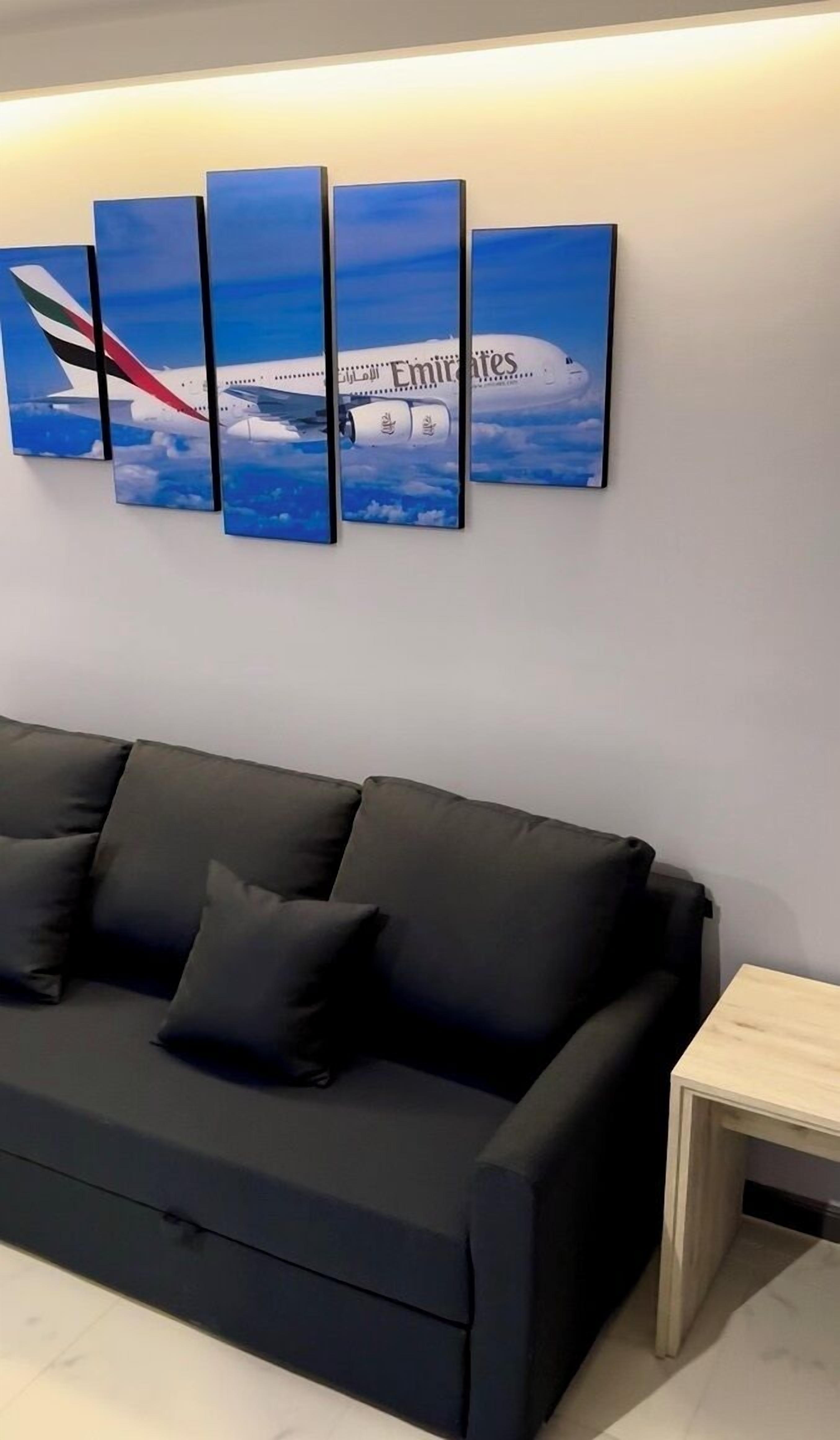 Un salon moderne avec un canapé noir et une œuvre d’art fixée au mur représentant un avion d’Emirates.