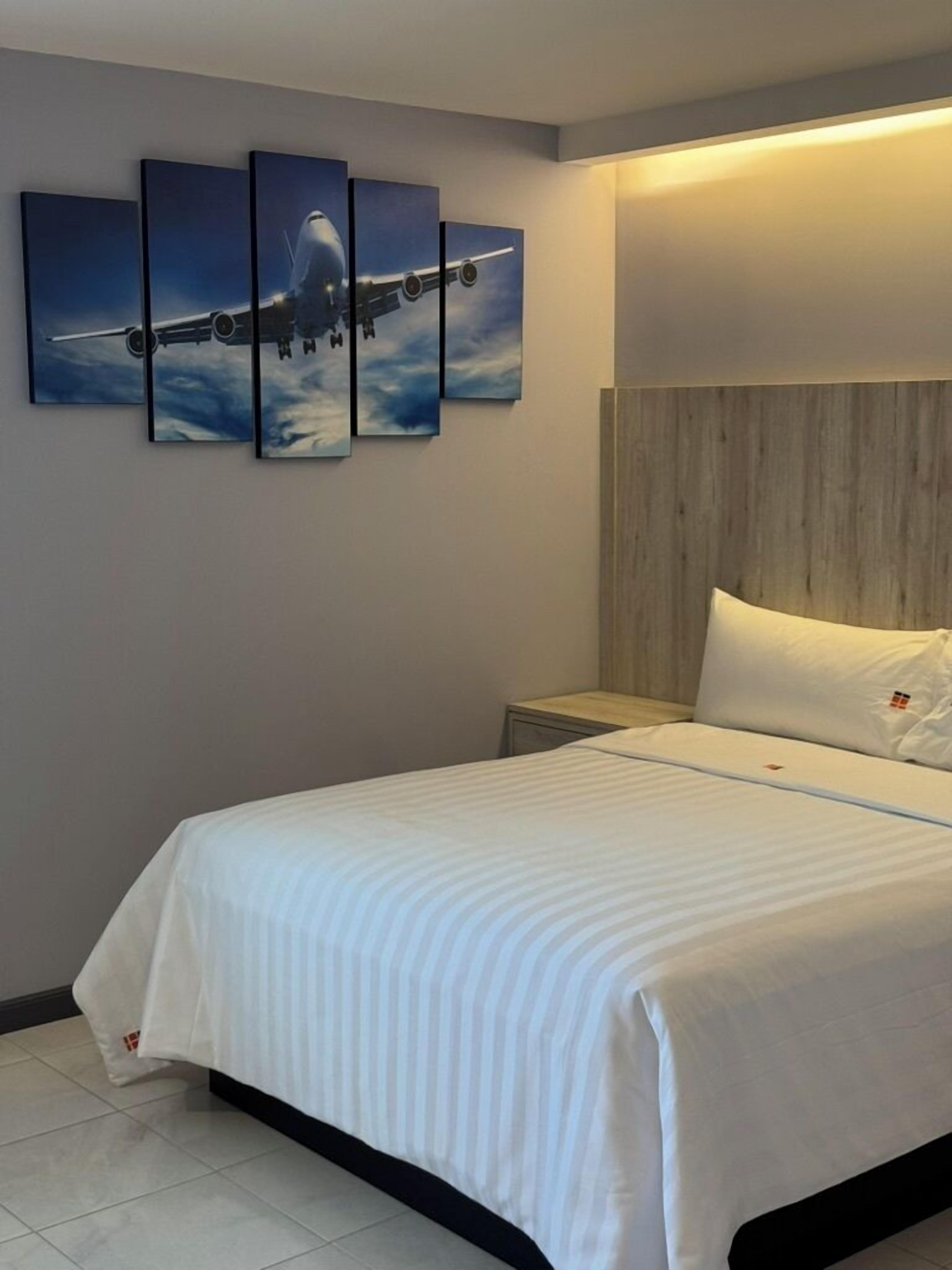 Ein Hotelzimmer mit einem großen Bett, einem Nachttisch und einem an der Wand befestigten Kunstwerk, das ein Flugzeug zeigt.