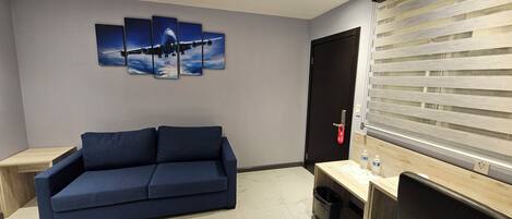 A modern living room with a blue sofa, a flat-screen TV, a wooden desk, and a wall-mounted airplane painting.