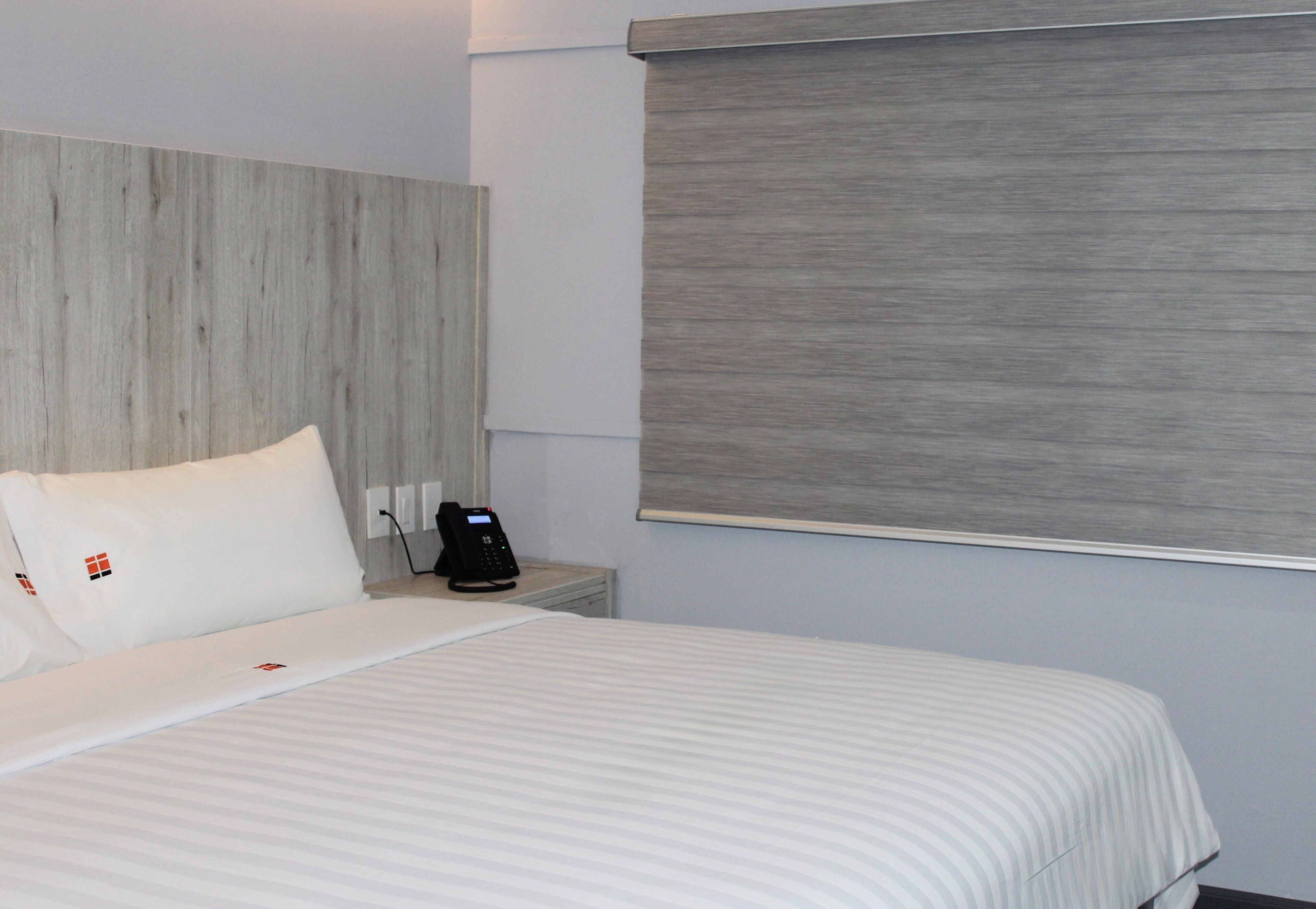 Une chambre d’hôtel avec un lit, une table de chevet avec un téléphone et une fenêtre avec un store.