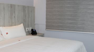Une chambre d’hôtel avec un lit, une table de chevet avec un téléphone et une fenêtre avec un store.