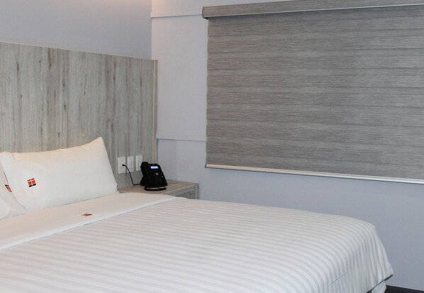 A hotel room with a bed, a bedside table with a phone, and a window with a blind. - Hangar Inn Tijuana (Tijuana)
