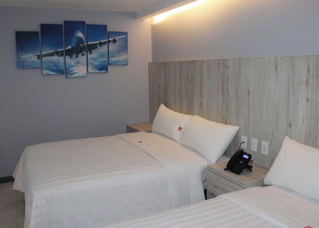 A hotel room with two beds, a wooden headboard, a phone on the nightstand, and a painting of an airplane on the wall.