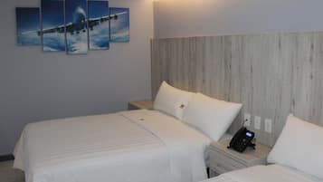 Quarto de hotel com duas camas, cabeceira de madeira, um telefone na mesa de cabeceira e um quadro de avião na parede.