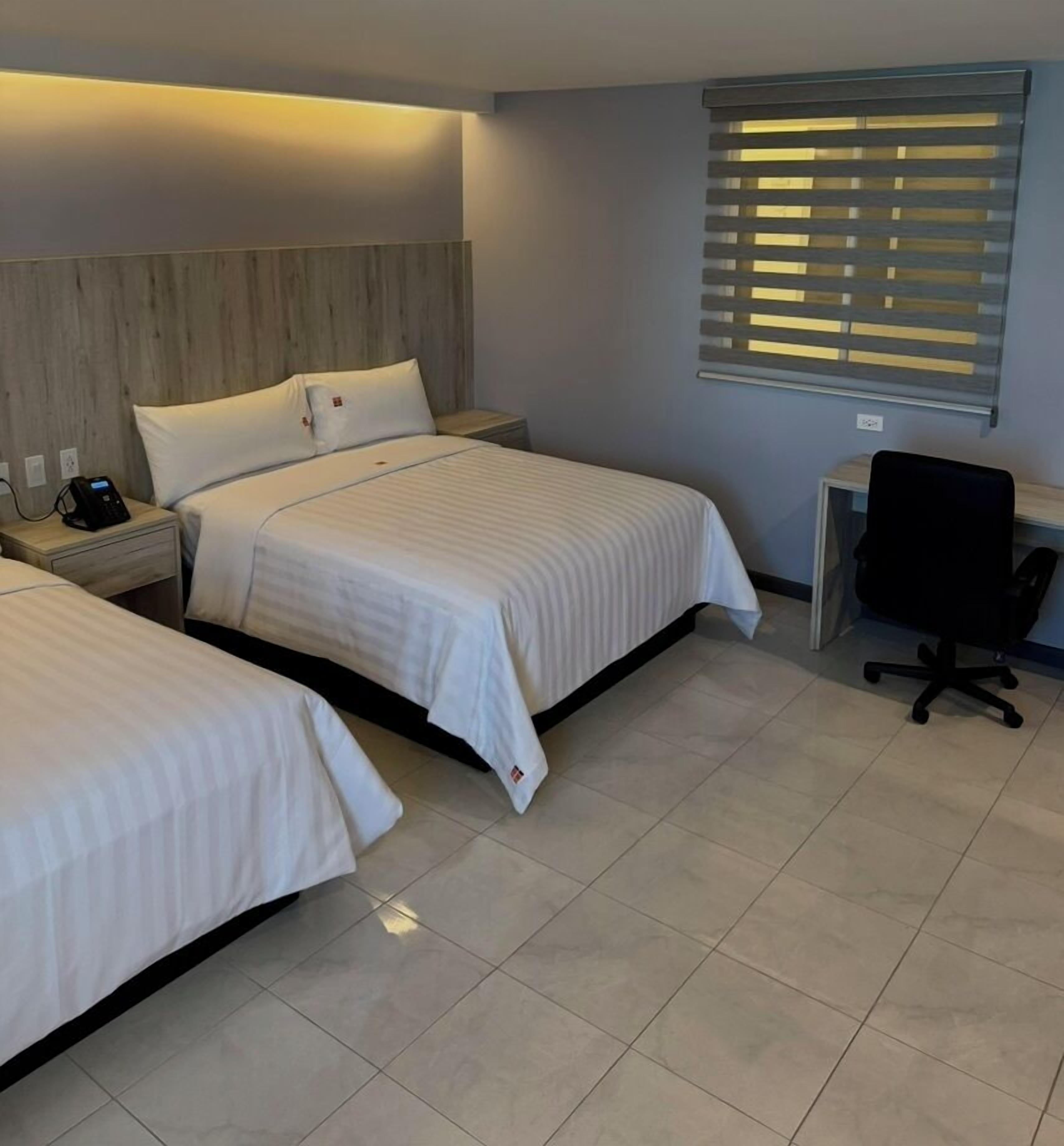 A hotel room with two beds, a desk, and a chair.