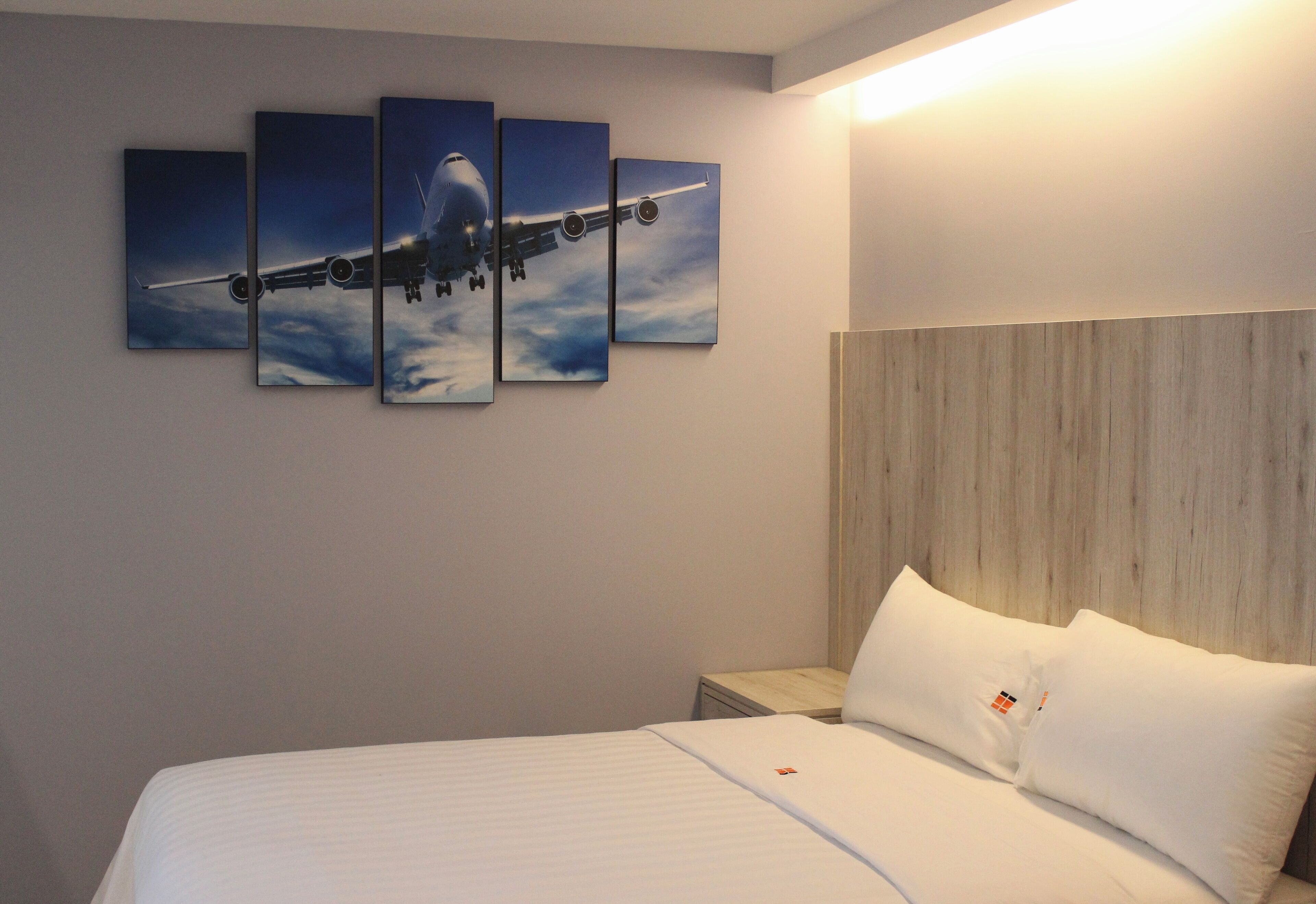A hotel room with a bed, a wooden headboard, and a wall with a multi-panel artwork of an airplane.