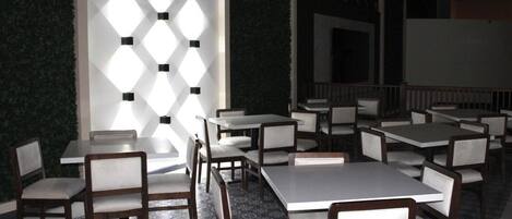 Un restaurante con varias mesas y sillas, suelo estampado y pared decorativa con iluminación geométrica.
