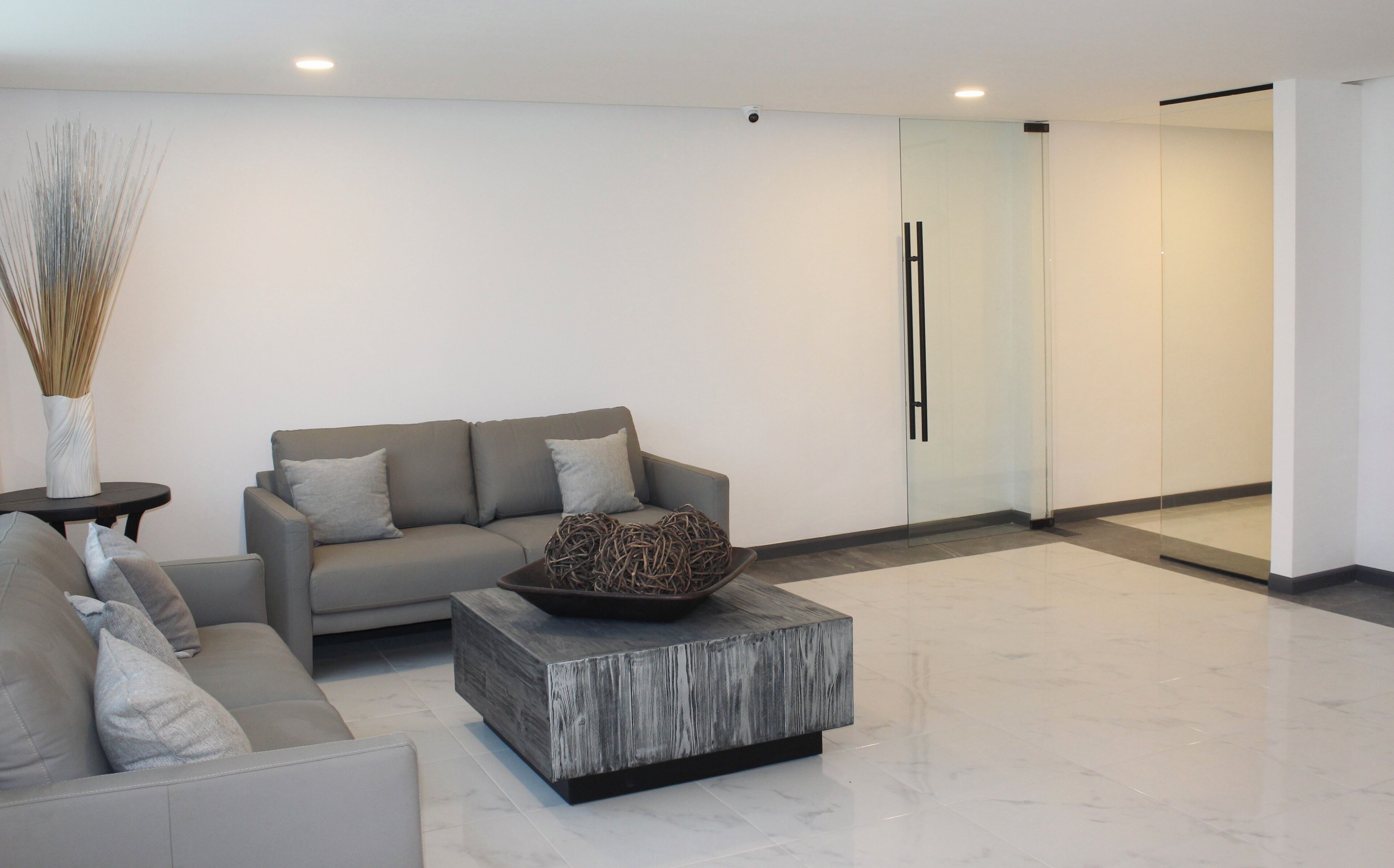 A modern living room with a grey sofa, a coffee table, and a vase with dried reeds.