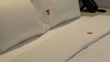 A neatly made bed with white bedding and a small logo on the pillow.