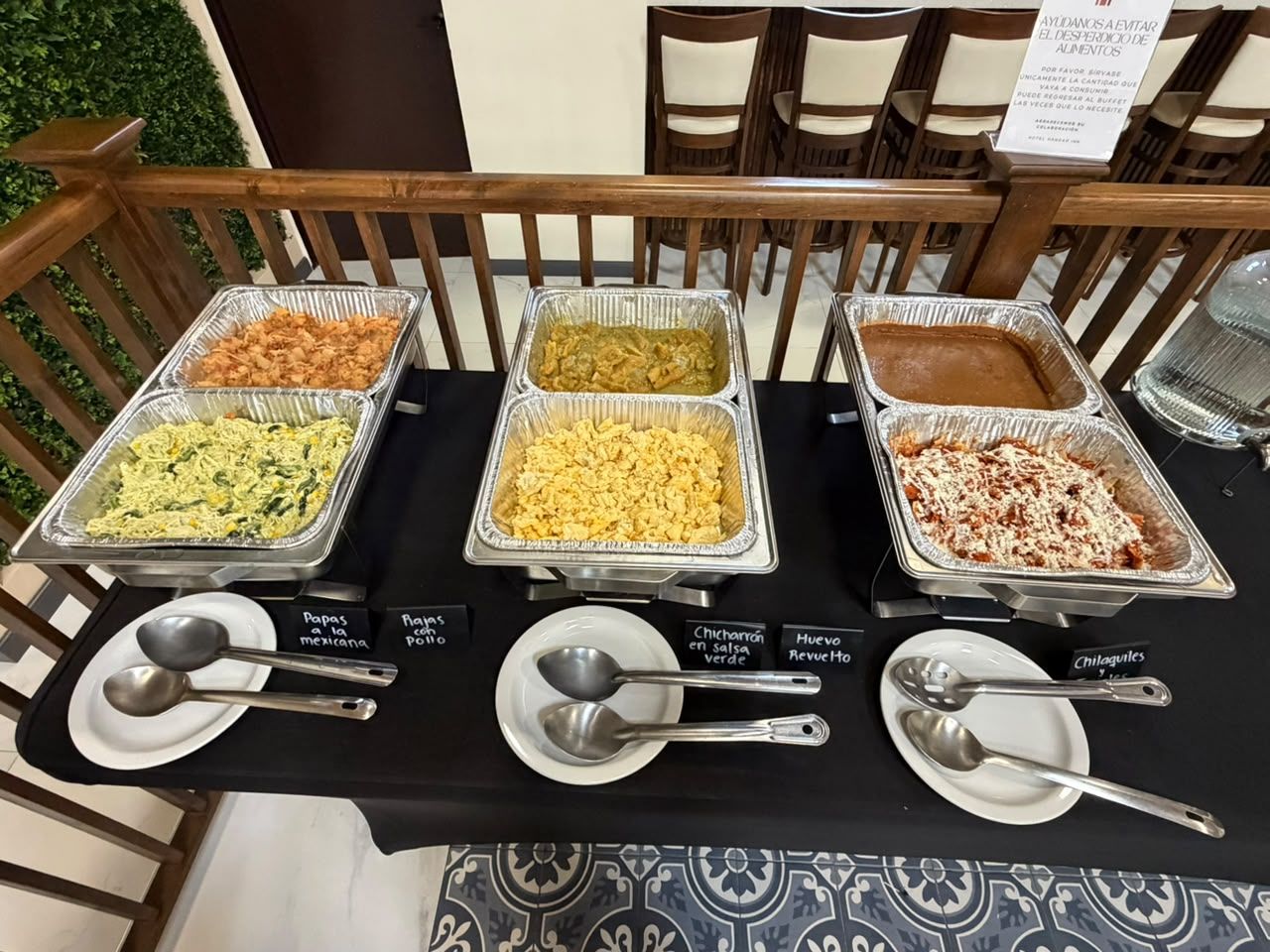 Une table de buffet avec des plats identifiés par des étiquettes et des ustensiles de service à disposition.
