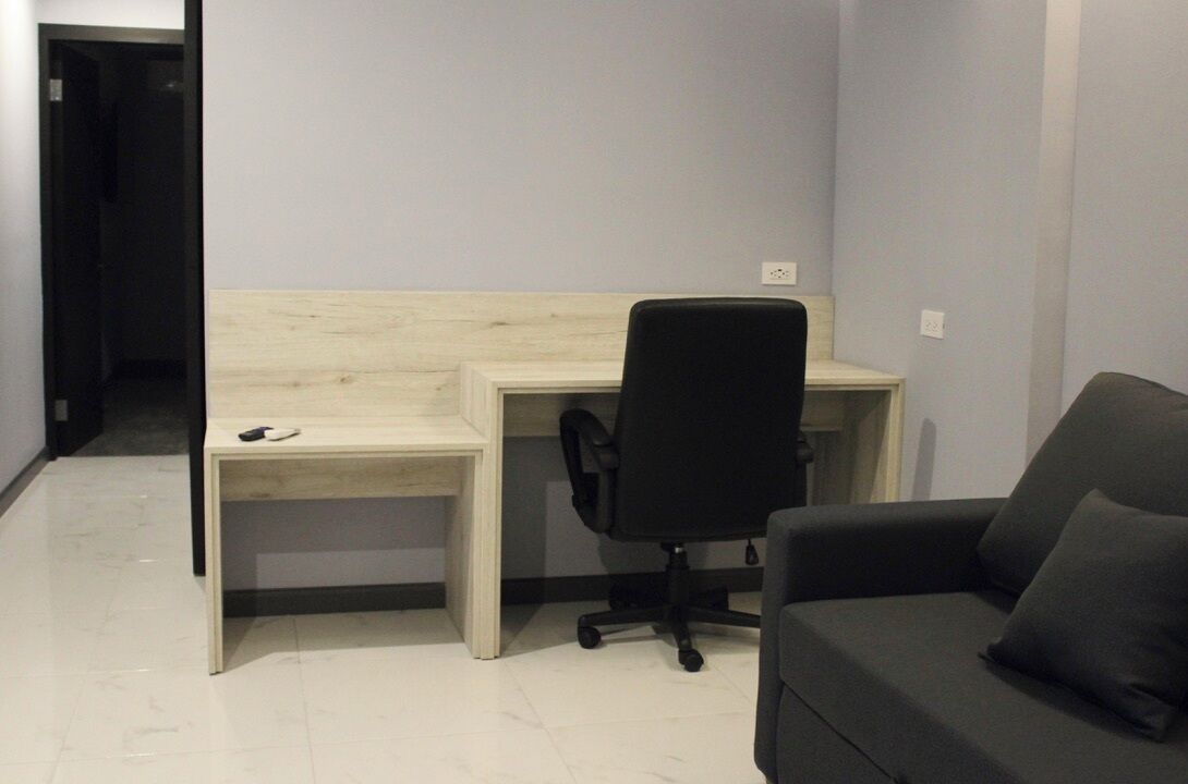 A small, modern room with a desk, a black office chair, and a dark sofa.