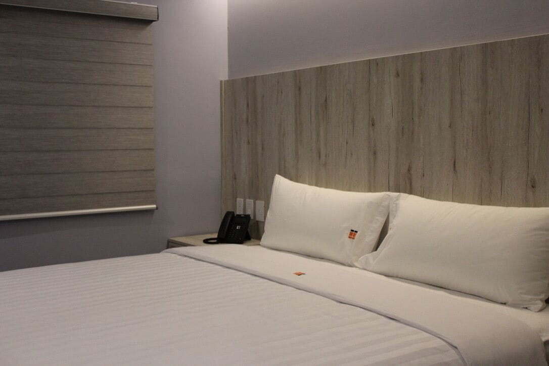 A hotel room with a wooden headboard, a bed with white bedding, and a bedside telephone.