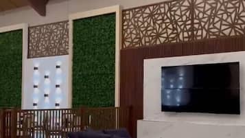 Una sala moderna con techo alto, un televisor de pantalla plana montado en una pared blanca, un sofá de color oscuro y un panel decorativo.