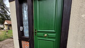 Een groene deur met een messing knokker, een raam met een bloemendecor en een bakstenen onderbouw.