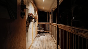A wooden porch with a bench and a small table, a door, and a wall with a heart-shaped decoration. - Nola Apartment (West Palm Beach)