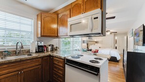 A compact kitchen with wooden cabinets, a microwave, a stove, and a sink. - Nola Apartment (West Palm Beach)