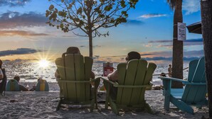 Two people seated on Adirondack chairs facing the ocean at sunset.