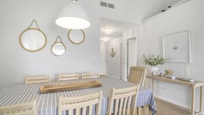 A dining area with a table set for four, wooden chairs, a hanging light fixture, and wall-mounted mirrors.
