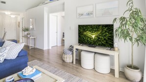 A modern living room with a blue sofa, a flat-screen TV, a large potted plant, and a wooden coffee table.