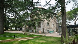 A stone building with a traditional architectural style, surrounded by a well-maintained grassy area and trees. - Espacio 1902 Sierra de Madrid (Collado Villalba)