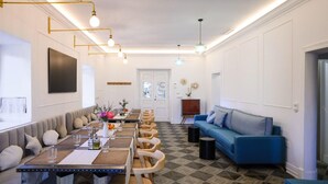 A modern dining area with a long table, cushioned seating, and a blue sofa. - Espacio 1902 Sierra de Madrid (Collado Villalba)
