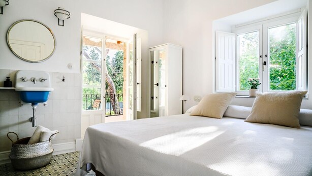 A bedroom with a bed, a round mirror, a blue sink, and a window with a view of greenery. - Espacio 1902 Sierra de Madrid (Collado Villalba)