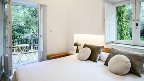 A bedroom with a large bed, two bedside tables, a nightstand, and a view of a balcony with outdoor furniture. - Espacio 1902 Sierra de Madrid (Collado Villalba)
